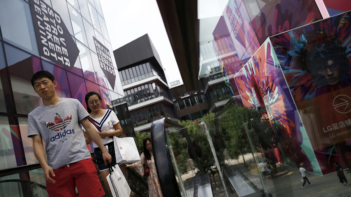 In this Sunday, July 15, 2018, photo, shoppers take escalator at the capital city's popular shopping mall in Beijing. Image credit: AP Photo/Andy Wong