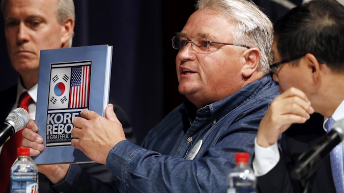 'We fought a war together,' says John Hall, a maintenance team member with Hyundai Motor Manufacturing Alabama, center, as he holds up a book about the Korean War, next to Joseph Boyle, senior director of business development and sales at LG Electronics, left, and Yong-Geun Kim, president and CEO of the Korean Automobile Manufacturers Association, during a Commerce Department hearing on investigation into whether auto imports threaten national security, Thursday, July 19, 2018, at the Commerce Department in Washington. Image credit: AP Photo/Jacquelyn Martin