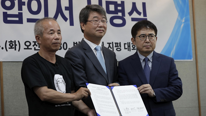 Hwang Sang-gi, left, father of former Samsung semiconductor factory worker Hwang Yu-mi who died from leukemia in 2007, Kim Ji-hyung, center, a chairman of the Mediation Committee and Kim Sunsig, right, senior vice president of Samsung Electronics, right, pose for the media during a signing ceremony in Seoul, South Korea, Tuesday, July 24, 2018. Image credit: AP Photo/Lee Jin-man