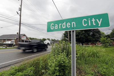 In this Tuesday, June 26, 2018, photo, Motorist drive past a Garden City sign, in Garden City, Ind. The collapse of Kiel Bros., which primarily operated under the name Tobacco Road, was widely publicized. For some families living near Columbus, the Kiel Bros. business left behind more than debt. They smelled oil in water drawn from private wells. Nearly three decades later, the unincorporated area known as Garden City is a federal Superfund site, a designation reserved for the nation’s most heavily polluted locations. (AP Photo/Darron Cummings)