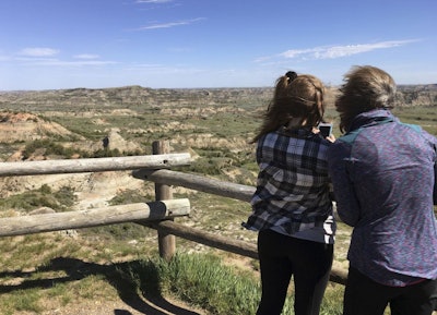 In this Wednesday, May 24, 2017, file photo, Jeanne Randall, right, and her daughter Zoe, of Shoreview, Minn., take photos at Painted Canyon in Theodore Roosevelt National Park in western North Dakota, near where a company wants to build an oil refinery about 3 miles from the park. A new study concludes visitors may be steering clear of some U.S. national parks or cutting their visits short because of pollution. (AP Photo/Blake Nicholson)