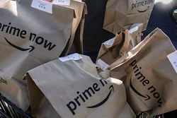 FILE - In this Feb. 8, 2018, file photo, Amazon Prime Now bags full of groceries are loaded for delivery by a part-time worker outside a Whole Foods store in Cincinnati. Amazon’s Prime Day deals are coming to the aisles of Whole Foods, as the online retailer seeks to lure more people to its Prime membership after recently hiking up the price. (AP Photo/John Minchillo, File)