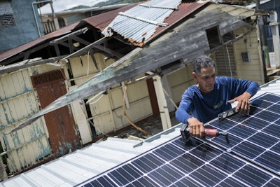 In this July 24, 2018 photo, Julio Rosario installs a solar energy system at a home in Adjuntas, Puerto Rico. The nonprofit environmental group Casa Pueblo has installed solar systems at two hardware stores, one barber shop, and several corner stores that activists hope will serve as a power oasis where people can charge their phones and store medications during a storm if needed. (AP Photo/ Dennis M. Rivera Pichardo)