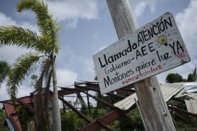 In this July 20 photo, a sign in Spanish that reads 'Attention government, AEE. Montones wants light. Six months without light,' hangs from a pole in Las Piedras, Puerto Rico. A scattering of hardware stores, barbershops and corner stores across the island are embracing solar energy, trying to wean themselves off a state-owned power company that remains heavily dependent on petroleum. (AP Photo/ Dennis M. Rivera Pichardo)