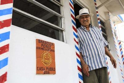 In this July 24, 2018 photo, barber Wilfredo Perez poses for a photo in front of his solar powered barber shop in Adjuntas, Puerto Rico. Perez says he can now open his barbershop 11 hours a day, six days a week thanks to the new system.(AP Photo/ Dennis M. Rivera Pichardo)