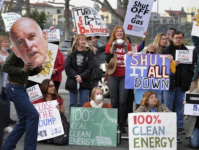 In this Jan. 16, 2016, file photo, protesters carry signs and an image of California's Gov. Jerry Brown while demanding a shut down of the Southern California Gas Company's Aliso Canyon Storage Facility near Porter Ranch in Los Angeles. A tentative settlement has been reached in litigation stemming from a leak at a Los Angeles storage field where a massive methane release forced thousands from their homes three years ago. (AP Photo/Richard Vogel)