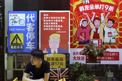 In this Monday, Aug. 13, 2018, photo, a man stands near a poster depicting a mural of U.S. President Donald Trump stating that all American costumers will be charged 25 percent more than others starting from the day president Trump started the trade war against China, on display outside a restaurant in Guangzhou in south China's Guangdong province. Image credit: Color China Photo via AP