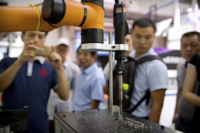 In this Aug. 15, 2018, photo, visitors look at a manufacturing robot from Chinese robot maker Aubo Robotics at the World Robot Conference in Beijing, China. Image credit: AP Photo/Mark Schiefelbein