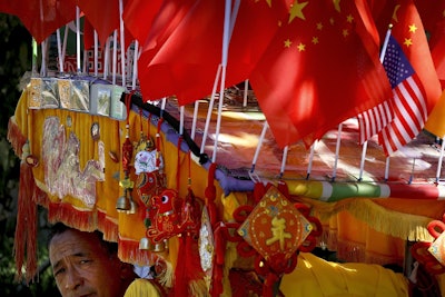 In this Sunday, Sept. 16, 2018, photo, a driver looks out from his trishaw decorated with an American flag and Chinese flags in Beijing. Image credit: AP Photo/Andy Wong