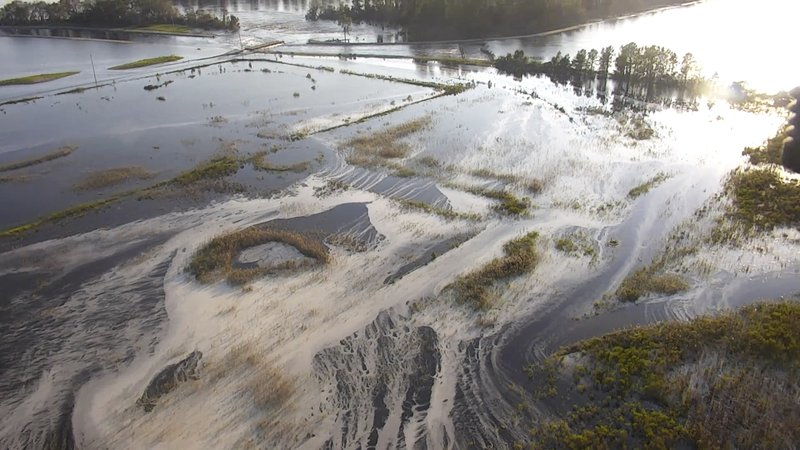 In this image made from Friday Sept. 21, 2018 drone video provided by the N.C. Department of Environmental Quality, light gray material flows out of a flooded coal ash dump toward the Cape Fear River at Duke Energy's L.V. Sutton Power Station in Wilmington, N.C. Floodwaters from Hurricane Florence breached a dam at the plant's 1,100 reservoir on Saturday, Sept 22, 2018, flooding a dump containing 400,000 cubic yards (305,820 cubic meters) of coal ash. The gray ash left over when coal is burned to generate electricity contains mercury, lead, arsenic and other toxic heavy metals. (N.C. Department of Environmental Quality via AP)