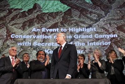 In this Jan. 9, 2012 file photo, then Interior Secretary Ken Salazar, center, standing in front of a map of the Grand Canyon, is applauded after announcing a twenty year ban on new mining claims near the Grand Canyon in Washington. Image credit: AP Photo/Jacquelyn Martin, File