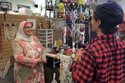 Former Iraqi refugee Nadeen Yousef, left, speaks to customers visiting her booth at the West Side Bazaar, where refugees sell clothes, crafts and food, Thursday, Sept. 27, 2018, in Buffalo, N.Y.