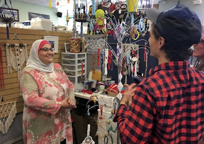 Former Iraqi refugee Nadeen Yousef, left, speaks to customers visiting her booth at the West Side Bazaar, where refugees sell clothes, crafts and food, Thursday, Sept. 27, 2018, in Buffalo, N.Y.