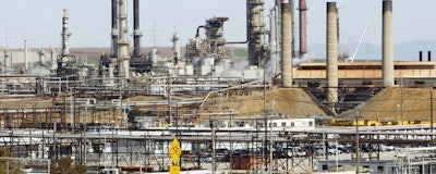 his March 9, 2010, file photo shows a tanker truck passing the Chevron oil refinery in Richmond, Calif. Federal officials say Chevron Corp. has agreed to pay a nearly $3 million fine and spend $160 million on environmental improvements and upgrading oil refineries to resolve allegations the company violated pollution laws. The U.S. Department of Justice announced the agreement Wednesday, Oct. 24, 2018. (AP Photo/Paul Sakuma, File)