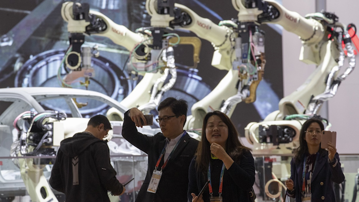 Attendees walk past robotic arms displayed at the China International Import Expo held in Shanghai, Monday, Nov. 5, 2018. Image credit: AP Photo/Ng Han Guan