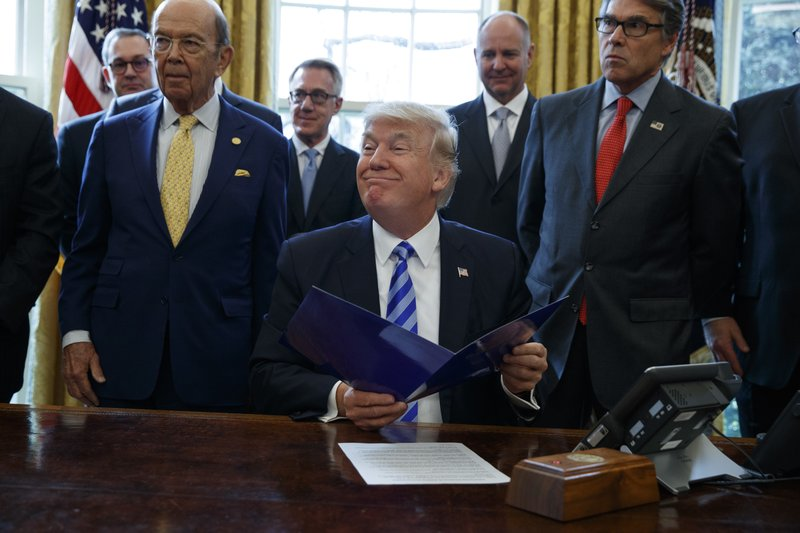 In this March 24, 2017 file photo, President Donald Trump, flanked by Commerce Secretary Wilbur Ross, left, and Energy Secretary Rick Perry, is seen in the Oval Office of the White House in Washington, during the announcing of the approval of a permit to build the Keystone XL pipeline, clearing the way for the $8 billion project.A federal judge in Montana has blocked construction of the $8 billion Keystone XL Pipeline to allow more time to study the project's potential environmental impact. U.S. District Judge Brian Morris' order on Thursday, Nov. 8, 2018, came as Calgary-based TransCanada was preparing to build the first stages of the oil pipeline in northern Montana. Environmental groups had sued TransCanada and The U.S. Department of State in federal court in Great Falls. (AP Photo/Evan Vucci)