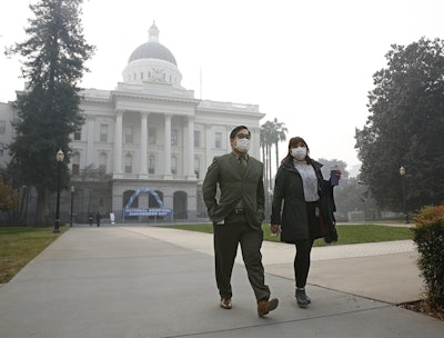 Tashi Nacario and Samantha Salas don masks to deal with the smoke from the Camp Fire that shrouds the state Capitol Thursday, Nov. 15, 2018, in Sacramento, Calif. Smoke from the blaze that burned through the Butte County city of Paradise is creating a health hazard that experts say could lead to an increase in serious health problems, especially for children and the elderly. (AP Photo/Rich Pedroncelli)