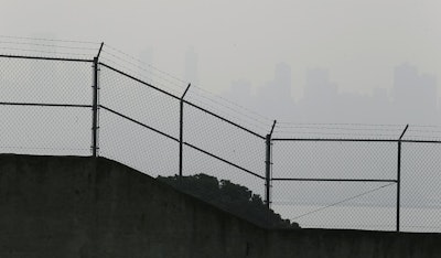 The skyline is obscured by smoke and haze from wildfires and is barely visible behind the prison exercise yard fence on Alcatraz Island Thursday, Nov. 15, 2018, in San Francisco. Recurring wildfires are sparking concern among medical experts about potentially major health consequences. Worsening asthma, lung disease and even heart attacks in heart disease patients have all been linked with previous fires. But blazes that used to be seasonal are happening nearly year-round and increasingly spreading into cities. That's exposing many more people to choking smoke that contains many of the same toxic ingredients as urban air pollution. (AP Photo/Eric Risberg)