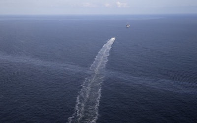In this March 31, 2015 aerial file photo, the wake of a supply vessel heading towards a working platform crosses over an oil sheen drifting from the site of the former Taylor Energy oil rig in the Gulf of Mexico, off the coast of Louisiana. A federal regulatory board has ruled that a New Orleans company can be required to perform more underwater drilling and excavation work to end a 14-year-old oil leak in the Gulf of Mexico. The Interior Board of Land Appeals refused to excuse Taylor Energy Company from requirements to permanently plug wells that could be leaking oil and gas. The board publicly released its Oct. 30 decision on Tuesday, Nov. 21, 2018. (AP Photo/Gerald Herbert)