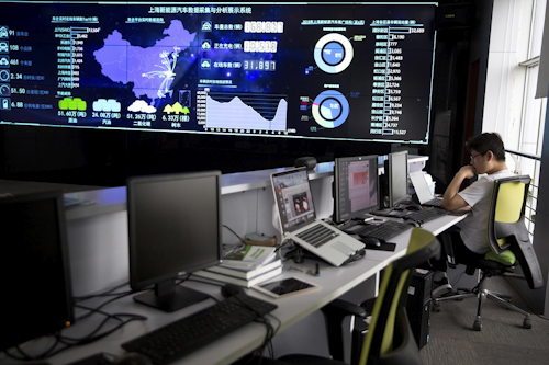 In this Friday, June 22, 2018, photo, a staff member looks at a laptop near a screen displaying live data from vehicles at the Shanghai Electric Vehicle Public Data Collecting, Monitoring and Research Center in Shanghai. Image credit: AP Photo/Ng Han Guan