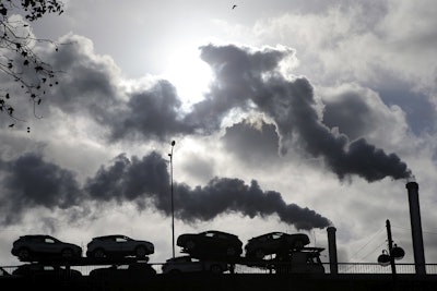 In this Friday, Nov. 30, 2018 file photo smoke rises from a factory as a truck loaded with cars crosses a bridge in Paris, France. Image credit: AP Photo/Michel Euler, File