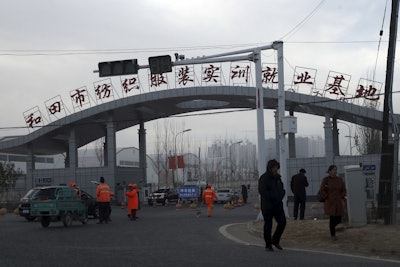 In this Wednesday, Dec. 5, 2018, photo, residents past by the entrance to the 'Hotan City apparel employment training base' where Hetian Taida has a factory in Hotan in western China's Xinjiang region. Image credit: AP Photo/Ng Han Guan