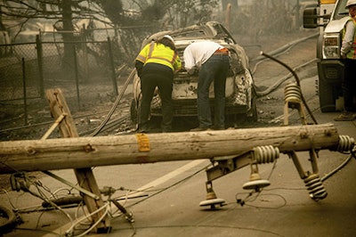 In this Nov. 10, 2018 file photo, with a downed power utility pole in the foreground, Eric England, right, searches through a friend's vehicle after the wildfire burned through Paradise, Calif. Facing potentially colossal liabilities over deadly California wildfires, PG&E will file for bankruptcy protection. The announcement Monday, Jan. 14, 2019, follows the resignation of the power company’s chief executive. (AP Photo/Noah Berger)