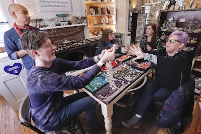 In this Thursday, Feb. 28, 2019, photo a customer at Allegory Gallery, Denise Glover, right, hands her selections to William Jones, one of the co-owners of the jewelry and art store, as fellow owner Andrew Thornton, left, talks with instructor Laurel Ross, center right, and client Cindy Kuhns, center left, in the small town of Ligonier, Pa. Image credit: P Photo/Keith Srakocic