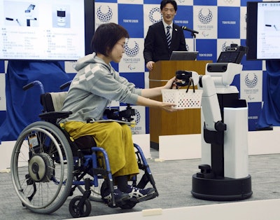 A robot passes a basket containing drinks to a woman in wheelchair during an unveiling event in Tokyo Friday, March 15, 2019. Image credit: Kyodo News via AP