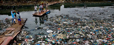 In this Sunday, Oct. 2, 2016 file photo, a man guides a raft through a polluted canal littered with plastic bags and other garbage in Mumbai, India. United Nations officials say nearly all of the world's countries have agreed on a deal to better manage plastic waste, with the United States a notable exception. A 'legally binding framework' that affects thousands of types of plastic waste emerged Friday, May 10, 2019 after a two-week meeting of U.N.-backed conventions on plastic waste and toxic chemicals. (AP Photo/Rafiq Maqbool)