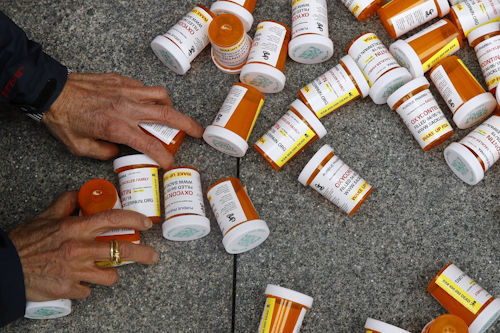 In this Friday, April 5, 2019, file photo, a protester gathers containers that look like OxyContin bottles at an anti-opioid demonstration in front of the U.S. Department of Health and Human Services headquarters in Washington, D.C. Image credit: AP Photo/Patrick Semansky