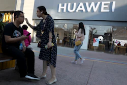 In this May 20, 2019, photo, a woman adjusts the glasses of a man outside a Huawei store in Beijing. Image credit: AP Photo/Ng Han Guan