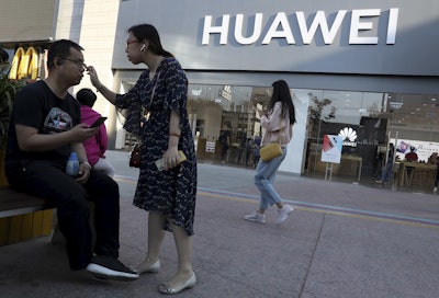 In this May 20, 2019, photo, a woman adjusts the glasses of a man outside a Huawei store in Beijing. Image credit: AP Photo/Ng Han Guan