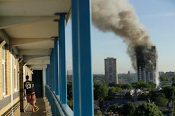 In this June 14, 2017, file photo, a resident in a nearby building watches smoke rise from a building on fire in London. Image credit: AP Photo/Matt Dunham, File