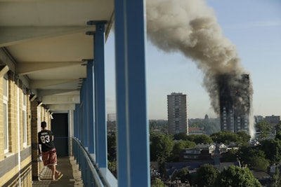In this June 14, 2017, file photo, a resident in a nearby building watches smoke rise from a building on fire in London. Image credit: AP Photo/Matt Dunham, File