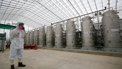 In this Nov. 12, 2014, file photo, a Tokyo Electric Power Co. (TEPCO) official wearing a radioactive protective gear stands in front of Advanced Liquid Processing Systems during a press tour at the Fukushima Dai-ichi nuclear power plant in Okuma, Fukushima Prefecture, northeastern Japan. Japan's economy and industry ministry has proposed gradually releasing or allowing to evaporate massive amounts of treated but still radioactive water at the tsunami-wrecked Fukushima nuclear plant. The proposal made Monday, Dec. 23, 2019, to a body of experts is the first time the ministry has narrowed down the options available to just releasing the water.