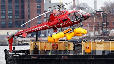 In this March 12, 2018 file photo, a helicopter, which crashed the previous day, is hoisted by crane from the East River onto a barge, in New York. The helicopter company, FlyNYON, exploited a regulatory loophole to avoid stricter safety requirements, federal investigators said Tuesday, Dec. 10, 2019.