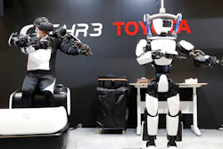 In this Dec. 18, 2019, photo, Toyota Motor Corp.'s human-shaped T-HR3 robot, right, is remotely controlled by its staff member, left, during a demonstration in Tokyo. Toyota's upgraded version of the human-shaped T-HR3 now has faster and smoother finger movements because the wearable remote-control device has become lighter and easier to use. The person wearing a headset and wiring made the robot move in exactly the same way he was moving, waving or making dance-like movements, as sensors sent computerized signals to the robot of what they detected as human movements.