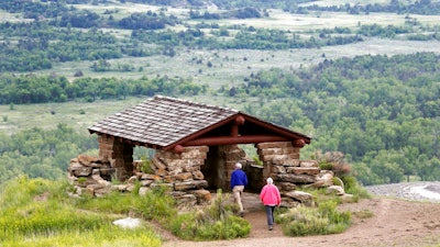In this June 11, 2014, file photo, visitors hike to a stone lookout over the Little Missouri River inside the Theodore Roosevelt National Park, located in the Badlands of North Dakota. Anemic funding, alleged unpaid work and legal fights are hobbling developers of a proposed $800 million oil refinery near the park in western North Dakota. But the project manager for Meridian Energy Group's Davis Refinery, which has drawn criticism from environmental groups and others who worry it would add to pollution near the national park, insists it will be built.