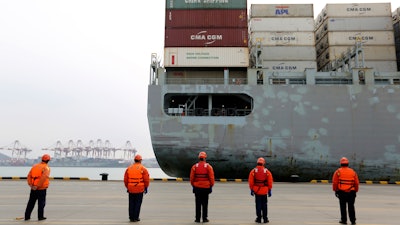 In this Tuesday, Feb. 4, photo, workers watch a container ship arrive at a port in Qingdao in east China's Shandong province. China cut tariffs on $75 billion of US imports including auto parts on Thursday, Feb. 6 in response to American reductions as part of their truce in a trade war.