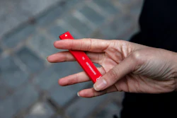 In this Jan. 31, 2020 photo a woman holds a Puff Bar flavored disposable vape device in New York. On Thursday, Feb. 6, 2020, the U.S. government began enforcing restrictions on flavored electronic cigarettes aimed at curbing underage vaping. But parents, researchers and students warn that some young people have already moved on to a newer kind of vape that isn't covered by the flavor ban - disposables.