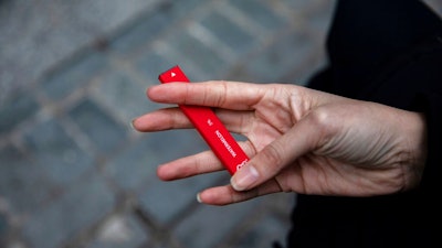In this Jan. 31, 2020 photo a woman holds a Puff Bar flavored disposable vape device in New York. On Thursday, Feb. 6, 2020, the U.S. government began enforcing restrictions on flavored electronic cigarettes aimed at curbing underage vaping. But parents, researchers and students warn that some young people have already moved on to a newer kind of vape that isn't covered by the flavor ban - disposables.
