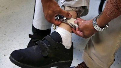 In this Aug. 13, 2014 file photo, a therapist checks the ankle strap of an electrical shocking device on a student during an exercise program at the Judge Rotenberg Educational Center in Canton, Mass.