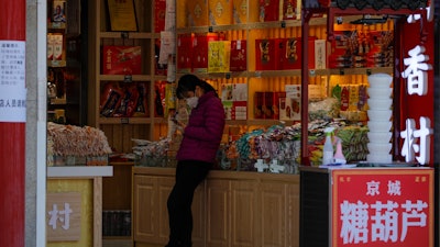 In this Tuesday, March 10, 2020, a staff wearing a protective mask browses her smartphone while waiting for customers at a shop at the Wangfujing shopping district following the coronavirus outbreak in Beijing.