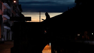 In this March 10, 2020 file photo, a woman wearing a face mask checks her phone as she walks at the Naviglio Grande canal in Milan, Italy.