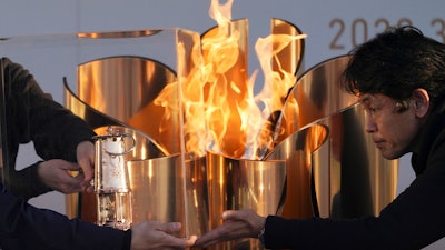 Officials light a lantern from the Olympic Flame at the end of a flame display ceremony in Iwaki, northern Japan, Wednesday, March 25, 2020.