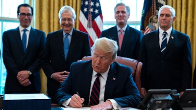 In this March 27, 2020 file photo, President Donald Trump signs the coronavirus stimulus relief package in the Oval Office at the White House.
