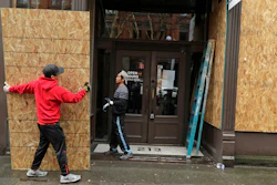Phu Dang, left, the owner of i5 Pho restaurant, gets help from a contractor as he boards up his business, Monday, March 30, 2020, in Seattle's downtown Pioneer Square neighborhood.