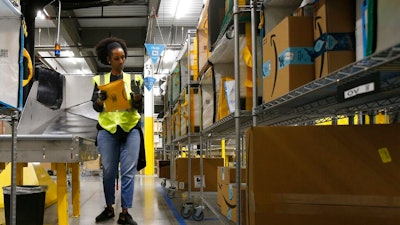 In this Dec. 17, 2019, file photo, Tahsha Sydnor stows packages into special containers after Amazon robots deliver separated packages by zip code at an Amazon warehouse facility in Goodyear, Ariz. On Monday, March 16, 2020, Amazon said that it needs to hire 100,000 people across the U.S. to keep up with a crush of orders as the coronavirus spreads and keeps more people at home, shopping online.