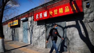A man wearing a protective face mask walks by shuttered business shops in Beijing, Sunday, March 1, 2020. Amid fears about where the next outbreak of a fast-spreading new virus would appear, infections and deaths continued to rise across the globe Sunday, emptying streets of tourists and workers, shaking economies and rewriting the realities of daily life.